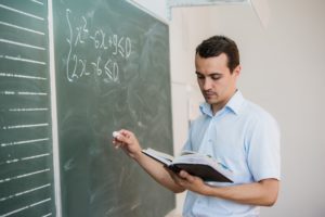 Young male teacher or student holding chalk writing on chalkboard in classroom